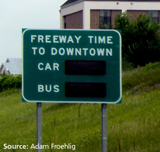 Photo of a signs designed to display travel time differences between private vehicle (car) and public transit (bus).