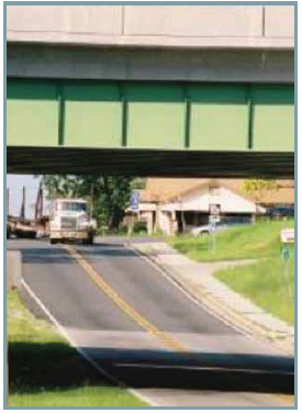 An empy lumber truck approaching a railroad overpass.