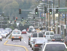 Photograph showing vehicles traveling through multiple traffic signals along a busy roadway.