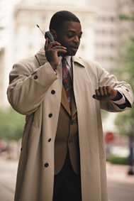 Photograph of a man looking at his watch while talking on his mobile telephone.