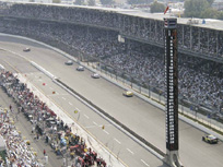 Photograph showing cars traveling around a racetrack while thousands of people look on from the stands.