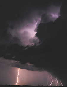 Photograph showing dark storm clouds in the sky and two bolts of lightening striking the ground.