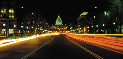 Photo of a busy road at night with the U.S. Capitol in the background.