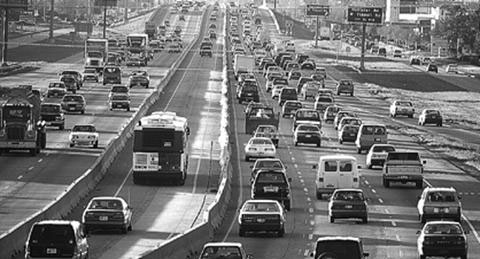 Figure 6: This photo shows the Katy (I-10W) HOV lane.  It shows the HOV lane is a one-lane, barrier-separated facility, located in the median of the Katy Freeway (I-10W).  A bus and two carpools are traveling in the HOV lane, while automobiles and other vehicles are traveling in the freeway lanes..  This figure helps the reader understand the design and operation of the Katy (I-10W) HOV lane.  The HOV lanes on all six freeways have the same design and operation characteristics.