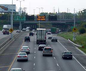 photo of one side of a divided highway with an overhead blank-out showing the message "TOO FAST FOR CURVE"