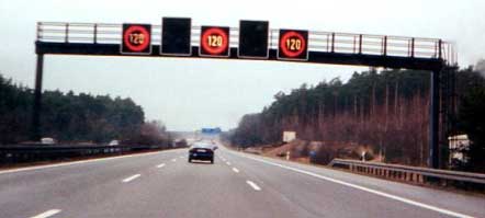 photo of a lane control installation. A variable speed limit sign is shown installed over each of three lanes. Each sign displays "120", the speed limit in kilometers per hour