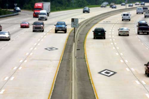 photo of concurrent HOV lanes on a highway showing a single lane provided in each direction of travel, located next to a median barrier, with no separation from the general purpose lanes; diamond-shaped HOV symbols are shown painted on the HOV lanes