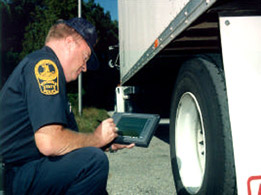 Photo of a State highway inspector using wireless hand-held computer next to a truck wheel.
