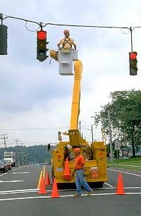 Two workers fixing a stoplight with one in a cherry picker.