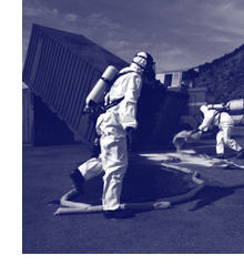 Photograph of a hazard response team dressed in full personal protective equipment, performing a contamination clean up.