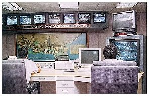 Photograph of two employees monitoring traffic on a number of CCTV displays and computer terminals at a TMC.