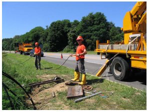 Photograph of workers installing underground communications cables beside a roadway.