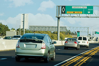 Photo. Cars driving on a highway, approaching an overhead sign marking exit lanes and southbound lanes, both for carpools only.