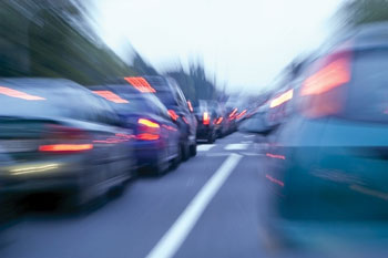 Photo. A blurred street-level view between cars showing heavy traffic congestion.
