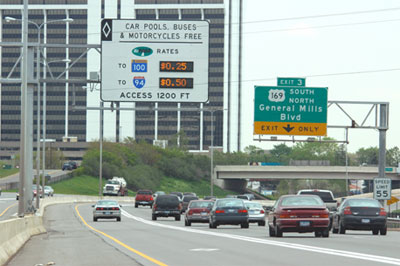 Image of Highway with High-Occupancy Vehicle (HOV) lane, showing sign for HOV lane indicating current tolls to go to two locations, and 'exit only' sign for general-purpose lanes.