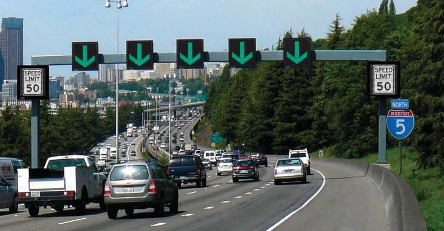 Photo of freeway in Washington State. An overhead gantry spans all five travel lanes, with an overhead lane-use control signal indication over each lane. The signs currently indicate all five lanes are open via steady downward green arrows. The overhead gantry also features variable speed limit signs on the side posts, which are set at 50 mph in the photo.