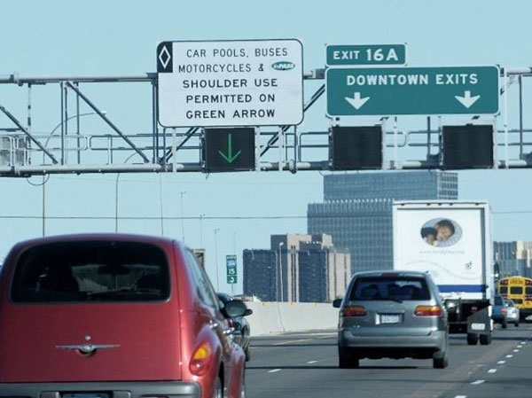 Photo of tandem static and dynamic message signs over a left-shoulder in Minneapolis. The static sign indicates carpools, buses, and motorcycles, and electronic transponder users may use the shoulder when the dynamic message sign displays a green arrow. The dynamic lane-control sign below displays a steady downward green arrow.