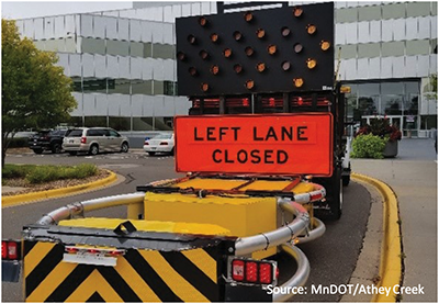 Photo of a MnDOT maintenance truck with truck-mounted attenuator equipped with connected arrow board with arrow activated and pointing to the right and sign showing left lane closed.