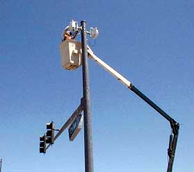 photograph of a worker in a bucket crane mounting a wireless system box at the top of a traffic signal support pole