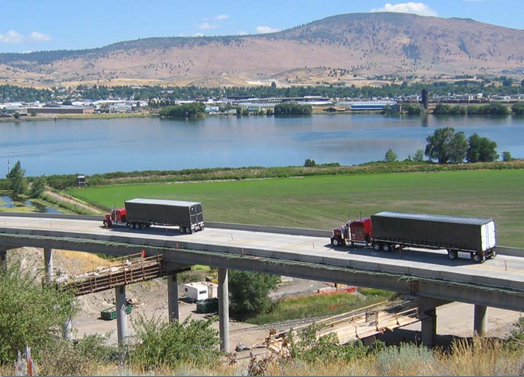 Image shows two cargo trucks on an overpass above a construction zone.