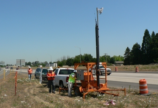 Image shows workers configuring road side equipment in a work zone.