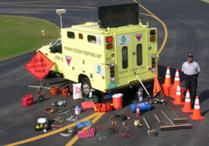 Photo of an operator standing next to a Highway Incident Response Unit with warning signs, traffic cones, and other equipment displayed behind the truck.