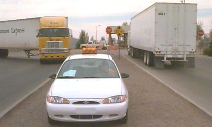 Photo of Outbound 1 data collection point, showing a truck entering the tollbooth and another exiting it. An official's car is in the foreground.