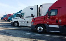 Various tractor trailers lined up in a truck parking area.