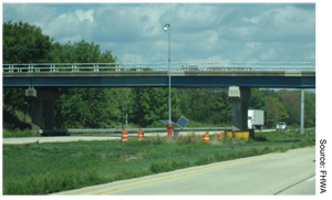 Figure 2. Temporary, Solar-Powered Traffic Detection and Camera Systems. Two photographs are provided, each showing a view of the light fixture pole with solar panels in the median of a divided highway. Source: FHWA