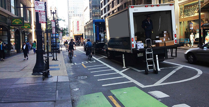 Delivery trucks in a hatched No Parking area, unloading along a protected bike lane