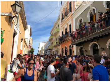 Crowds fill a narrow street and hang off balconies overlooking festival goers.