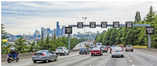 A series of variable message signs are posted on a gantry above four lanes of traffic. A sign is mounted above each lane.