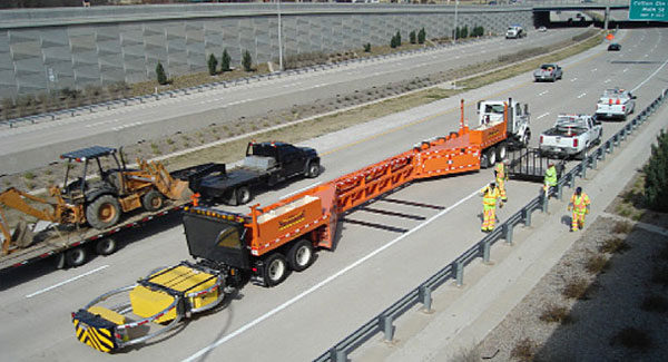 This photo shows a mobile barrier system set up in the right lane of a highway, shielding a maintenance crew working in the right shoulder.