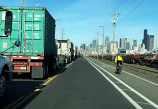 photo of lone bicylist in a bike lane adjacent to a lane of trucks backed up in traffic