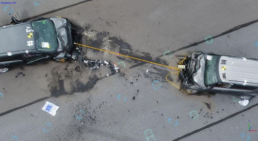 An aerial photo taken with unmanned aircraft systems of a car crash scene with 2 cars that had a head on collision and a line drawn between the hoods of the two cars measuring the distance.