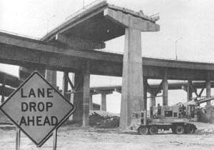 photo of warning sign stating "lane drop ahead" next to unfinished highway bridge construction