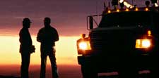 two workers silhouetted in the beam of a work vehicle's headlights