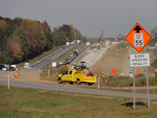 A construction work zone displaying an orange diamond shape sign with the wording SPEED LIMIT 55 with an arrow pointing upward and a horizontal rectangular sign below it with the wording $50 SPEEDING PENALTY.
