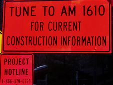 An image displaying two traveler information work zone signs. The first sign displays: TUNE TO AM 1610 FOR CURRENT CONSTRUCTION INFORMATION. The second sign displays: PROJECT HOTLINE 1-866-879-0395.