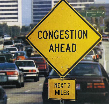 Photograph showing a yellow, diamond shaped sign with the words "Congestion Ahead" on it. Below the diamond-shaped sign is a smaller sign that says "next two miles" on it.