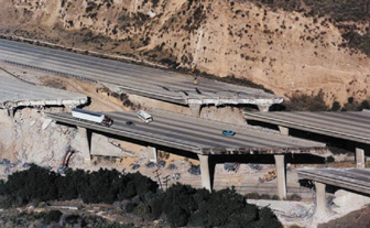 Photograph showing two adjacent highway bridges along a hillside. Both highways appear to have broken into several pieces due to a natural disaster, such as an earthquake.