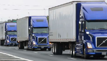An image of three blue freight trucks on a multi–lane road.