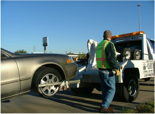 This photo shows a tow truck preparing to tow a disabled vehicle from a freeway shoulder.