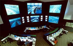 Figure 1-1 MD CHART Traffic Management Center: a large room with a high ceiling includes a wall of 6 giant video screens that show different live traffic scenes