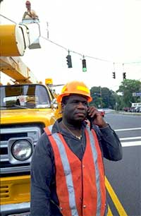 Figure 1-2 INFORM Operator I-495 Long Island: man dressed in an orange safety vest and hardhat makes a cell phone call from an intersection controlled by traffic signals