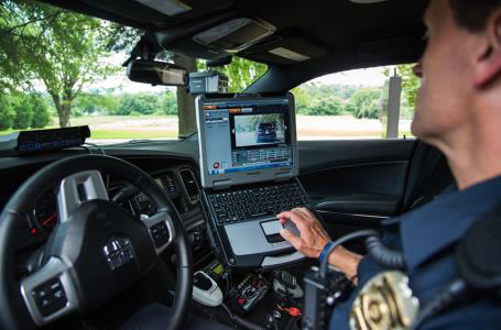 Police officer in car viewing laptop.