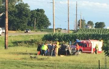 Site of fatal crash on rural road.  EMTs surround car that is off the road.