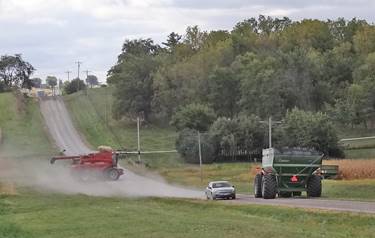 A car and farm equipment share a gravel road.