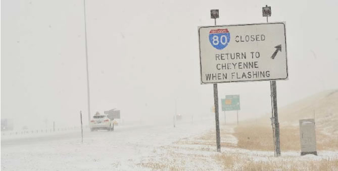 Snowy road with single car on it with a Road sign that says 'I80 Closed Return to Cheyenne when flashing#39;