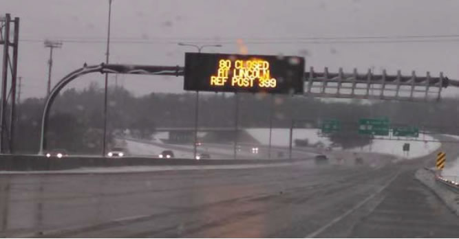 Snowy interstate road with overhead sign that reads '80 closed at Lincoln ref post 399'
